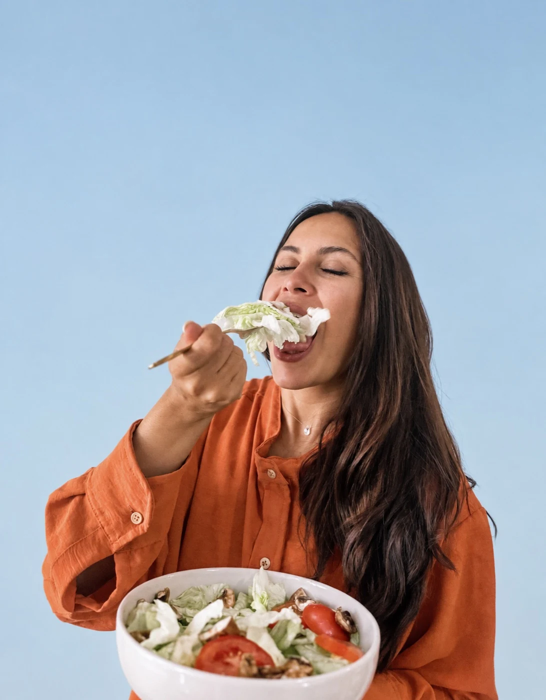 Iliana disfrutando un bocado de ensalada, con fondo celeste