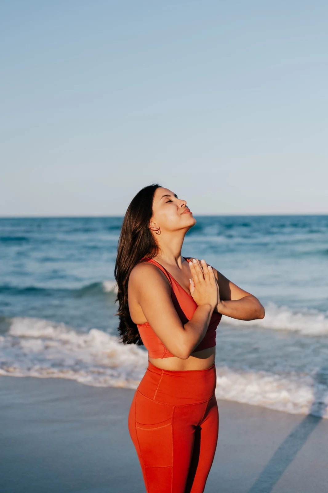 Iliana con las manos juntas y el rostro hacia el cielo frente al mar